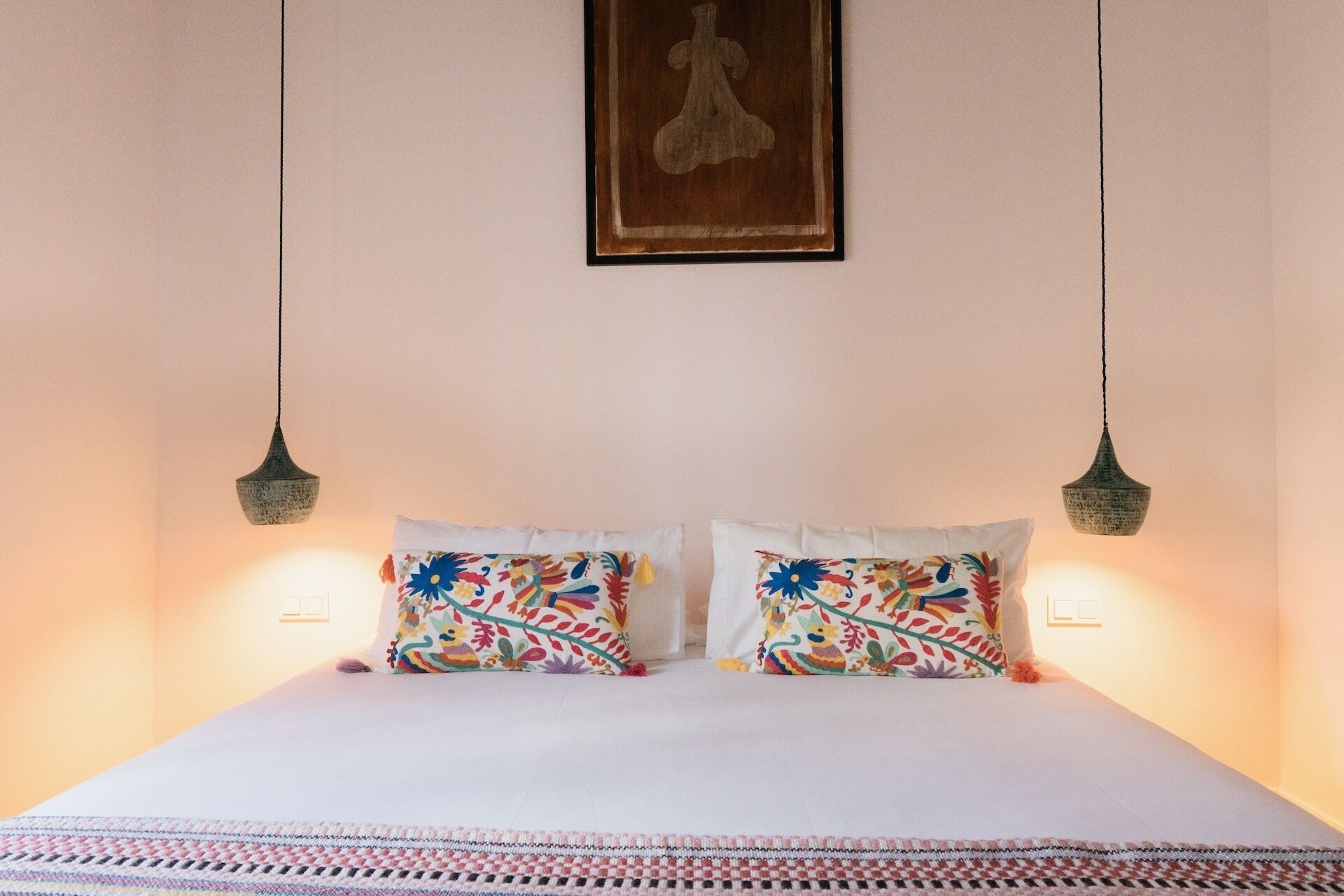 A bed with two pillows, a hanging light fixture, and a framed picture on the wall.