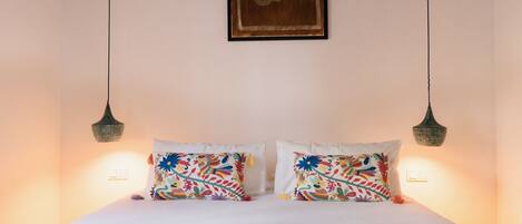 A bed with two pillows, a hanging light fixture, and a framed picture on the wall.