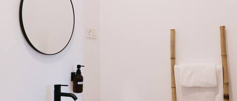 A bathroom with a white sink, a round mirror, a black faucet, and a bamboo ladder with towels.