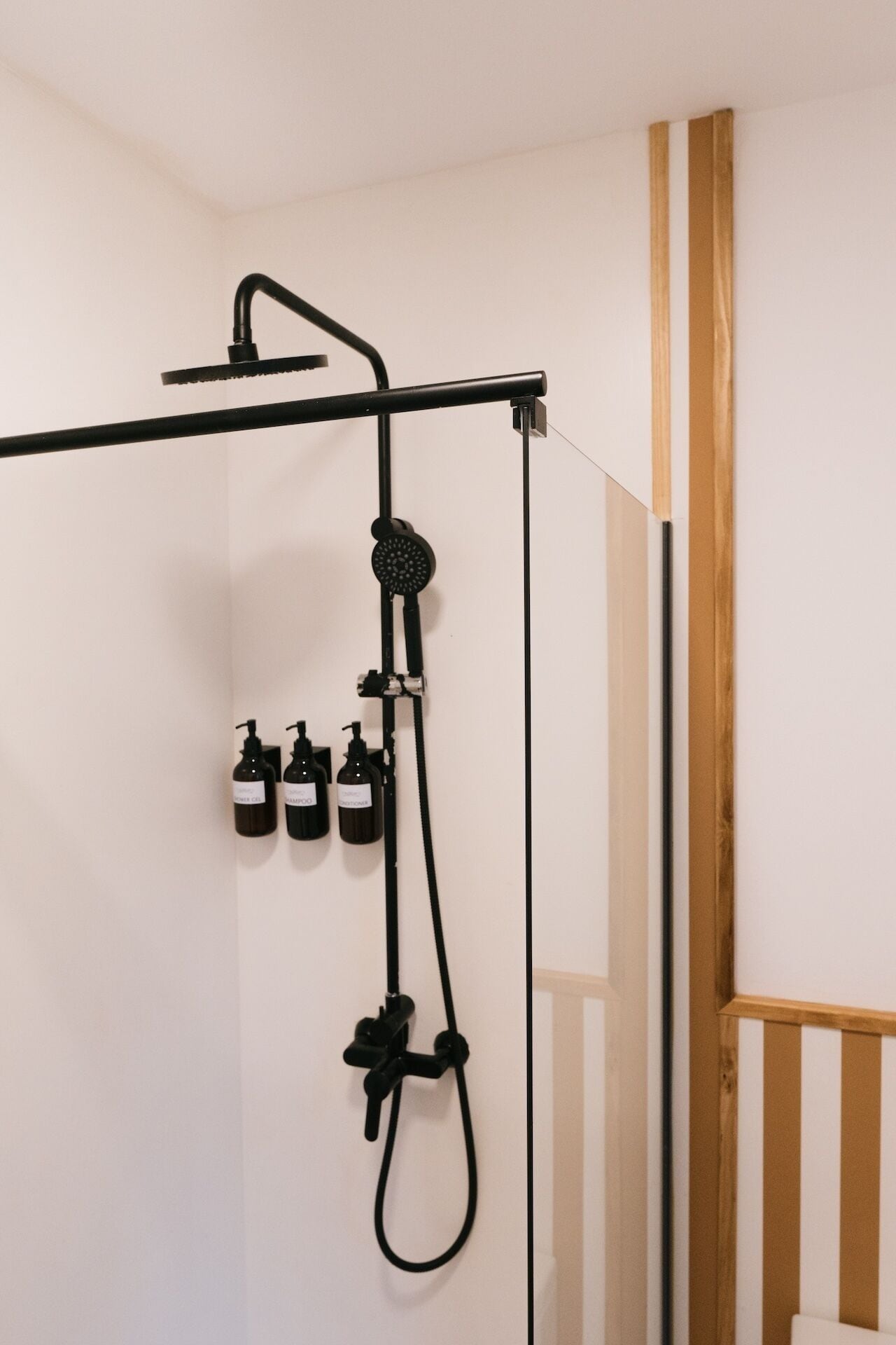 Une salle de bain moderne équipée d’un système de douche comprenant un pommeau de douche à main, une pomme de douche à pluie et plusieurs flacons de shampoing et d’après-shampoing.