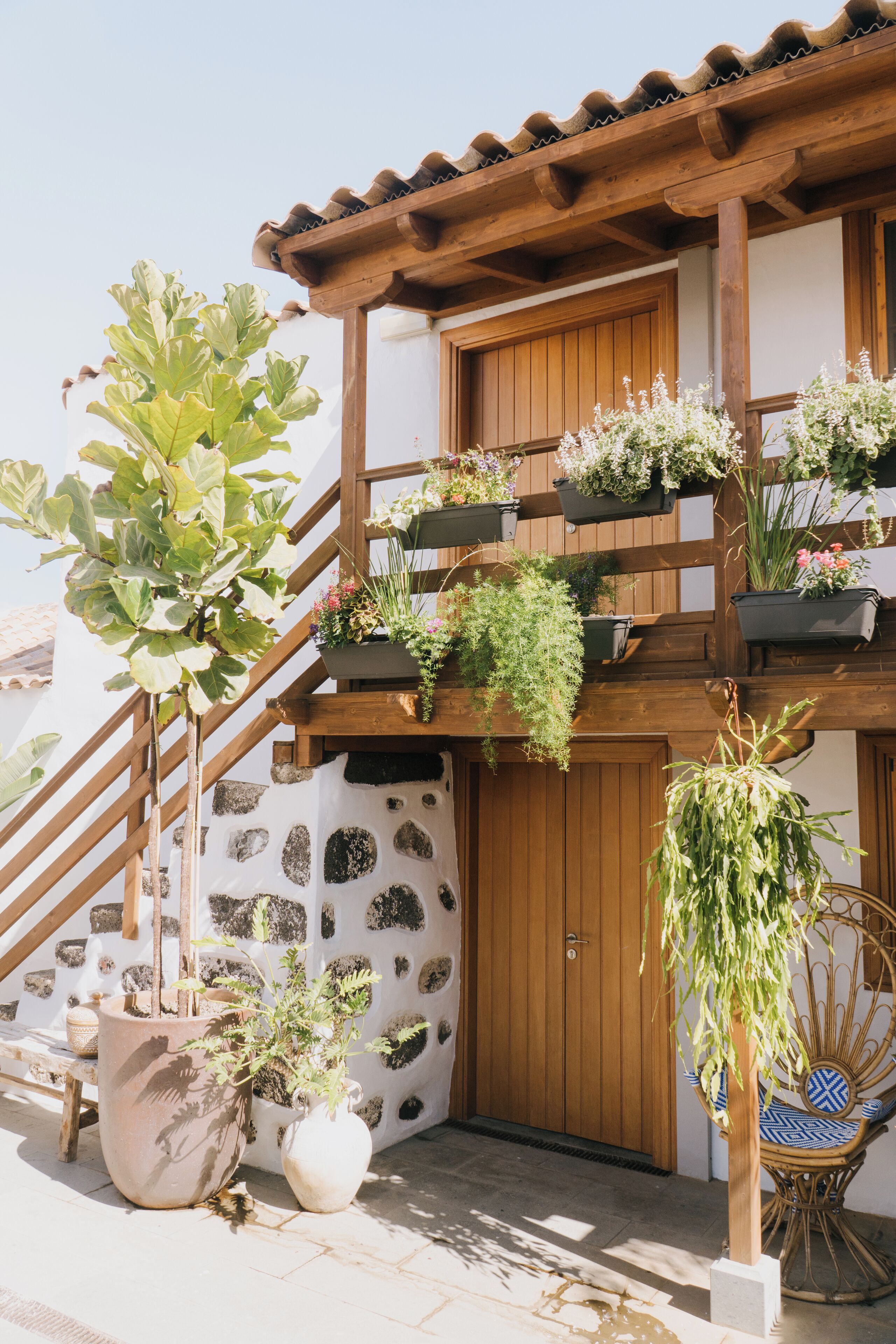 A wooden balcony with potted plants and a wicker chair.
