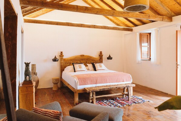 A bedroom with a wooden bed, a small stool, a chair, a wooden floor, and a window. - Dreamsea Gran Canaria Boutique (Moya)