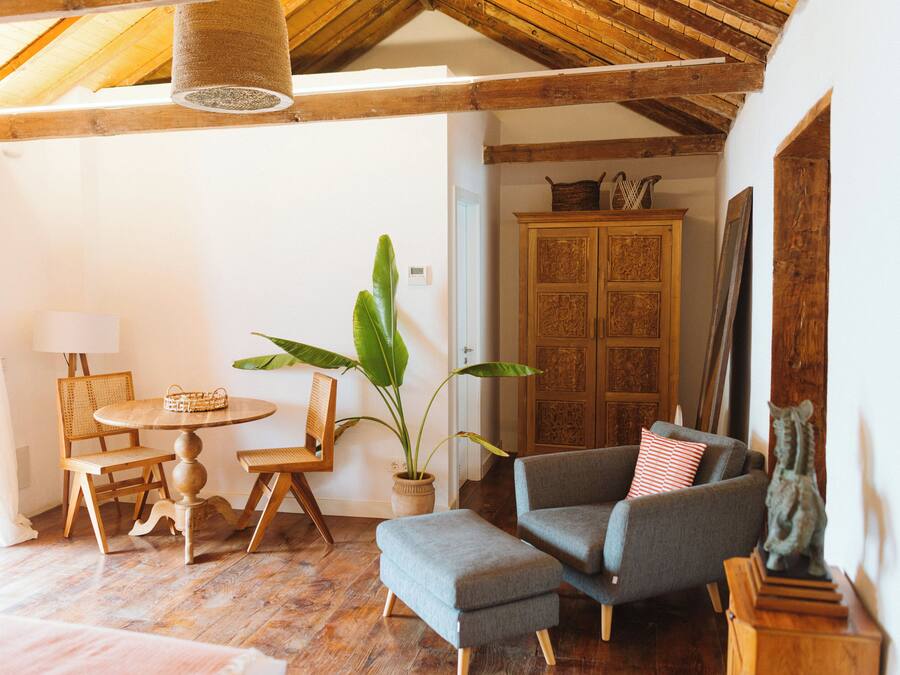 Una habitación acogedora con techo de madera, una mesa redonda de madera con sillas, un sofá gris, una planta en maceta y un armario con puertas.