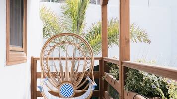 Een houten balkon met een rieten stoel en een tafel, omringd door houten leuningen en plantenbakken.