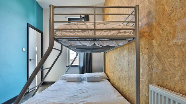 A bunk bed with a metal frame, white bedding, and a wooden wall. - Studio 95 - Shared & Private Rooms (Swansea)