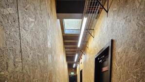 A narrow hallway with wooden walls and a grey floor, leading to a black door with a 'PLAY' sign. - Studio 95 - Shared & Private Rooms (Swansea)