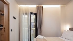 A modern hotel room with a bed, a shower area, and a view through a glass door. - Award-Winning Chic Apartment · Steps from Beach & Old Town · Sleeps 5 (Rethymno)