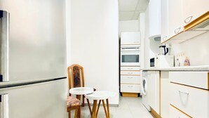 A modern kitchen with white cabinetry, a built-in oven, a microwave, and a coffee maker. There is a small round table with two chairs. - Sweet 3BR Apt in a Quiet Neighborhood (Vienna)
