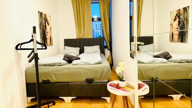 A hotel room with two beds, a standing mirror, a small table with a vase, and a window with curtains. - Sweet 3BR Apt in a Quiet Neighborhood (Vienna)