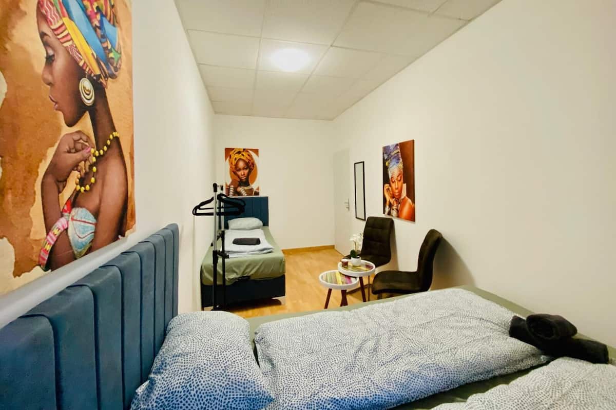 A hotel room with a bed, a chair, a small table, and artwork on the walls.