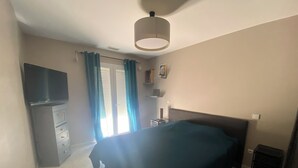 A bedroom with a bed, a TV, a dresser, and a window with curtains.