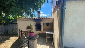 An outdoor kitchen area with a stone floor, a pink potted plant, and a chimney.