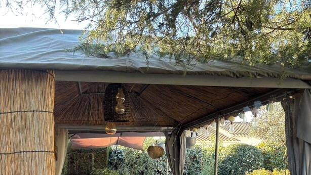 Un patio al aire libre con una mesa y sillas de madera, rodeado por un muro de paja y cubierto por un techo.