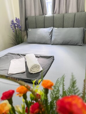 A neatly made bed with grey linens, a rolled white towel, and a folded white towel on the bed. - Shore 3 1 BR 1006 (Pasay)
