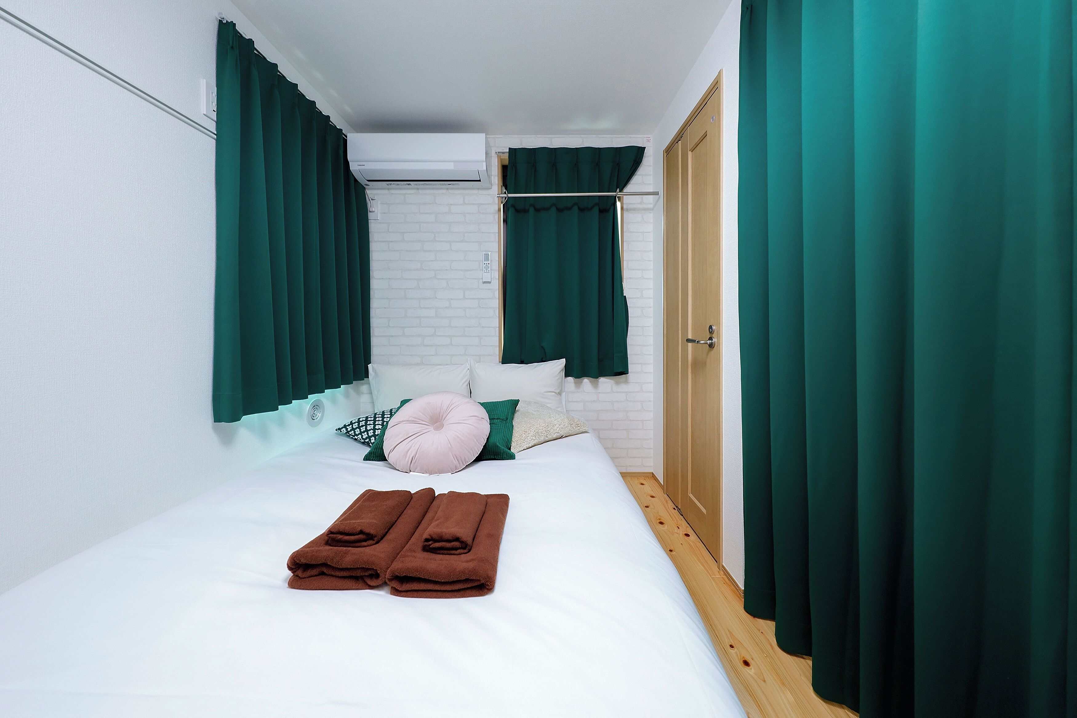 A neatly made bed with green curtains, a white brick wall, and a wooden floor.