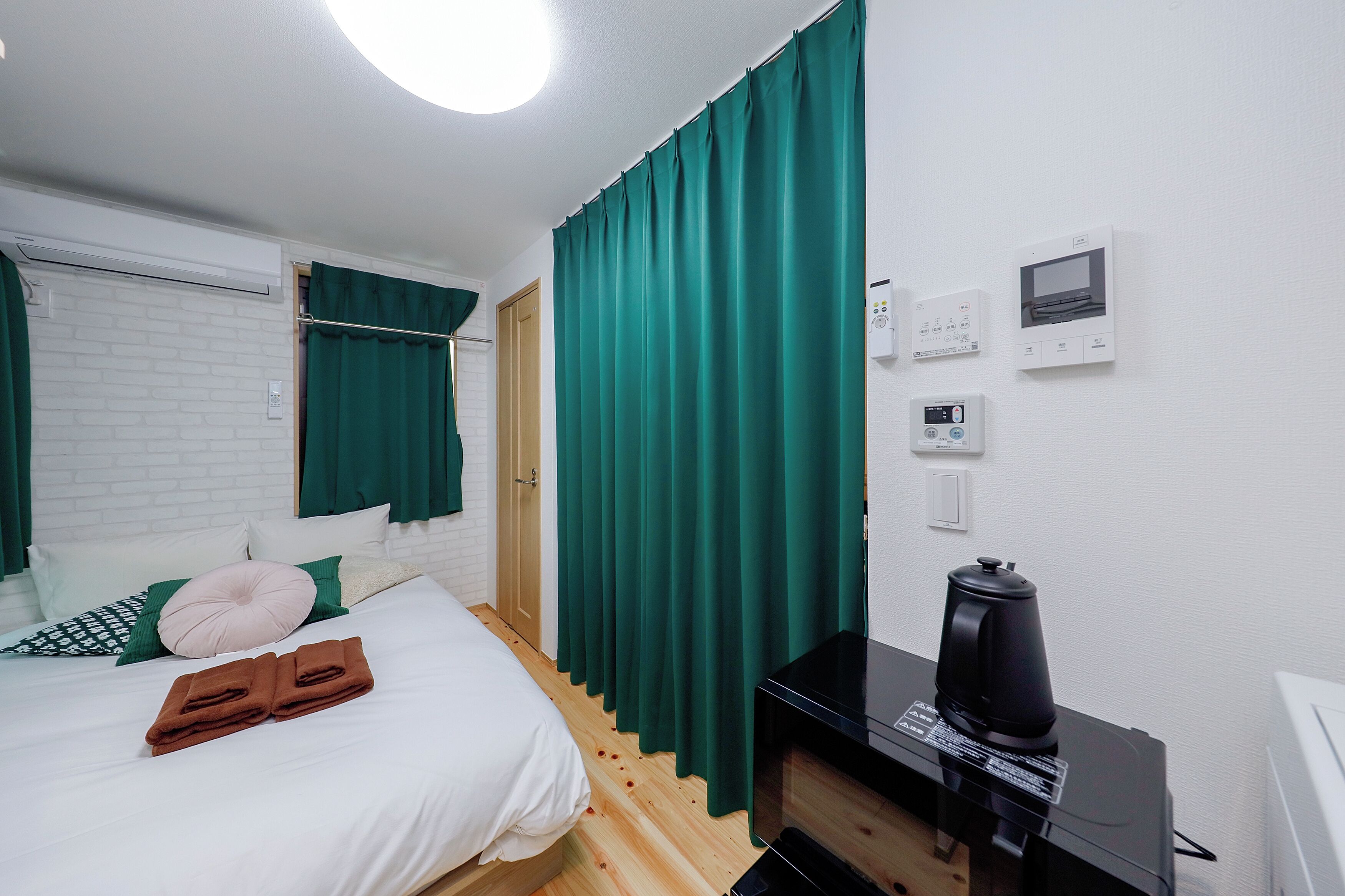 A hotel room with a bed, green curtains, a coffee maker, and a thermostat on the wall.