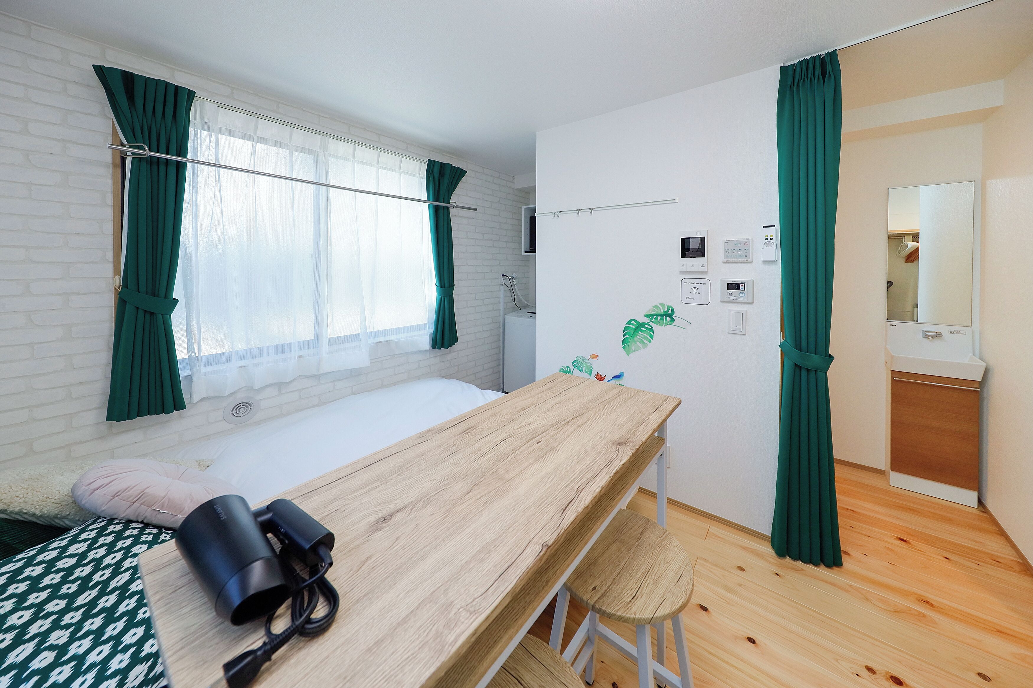 Une chambre avec un lit en bois, un bureau et une chaise. Il y a une fenêtre avec des rideaux, un téléviseur fixé au mur et une petite plante.