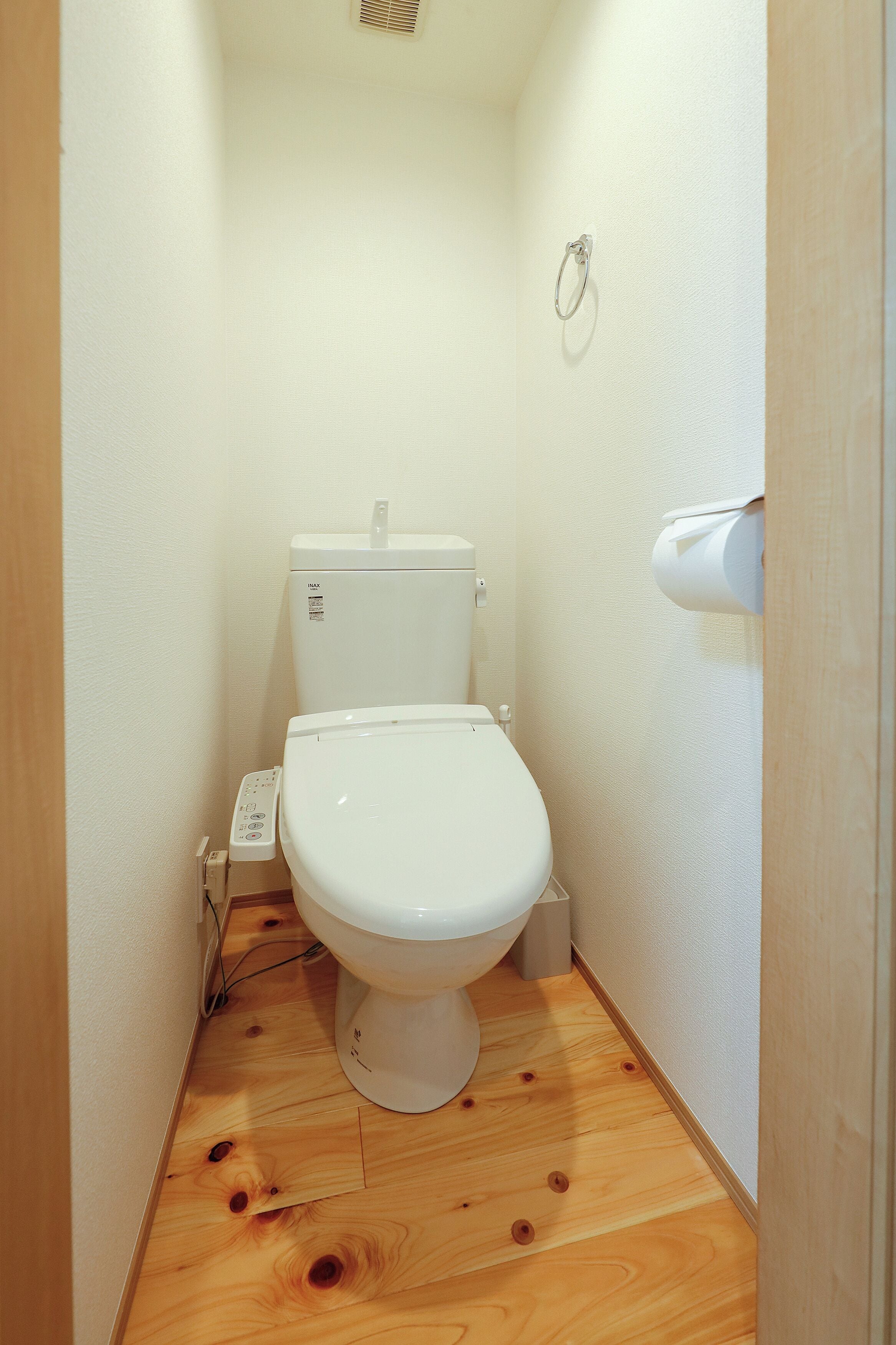 A small, narrow bathroom with a white toilet, a wooden floor, and a white wall.