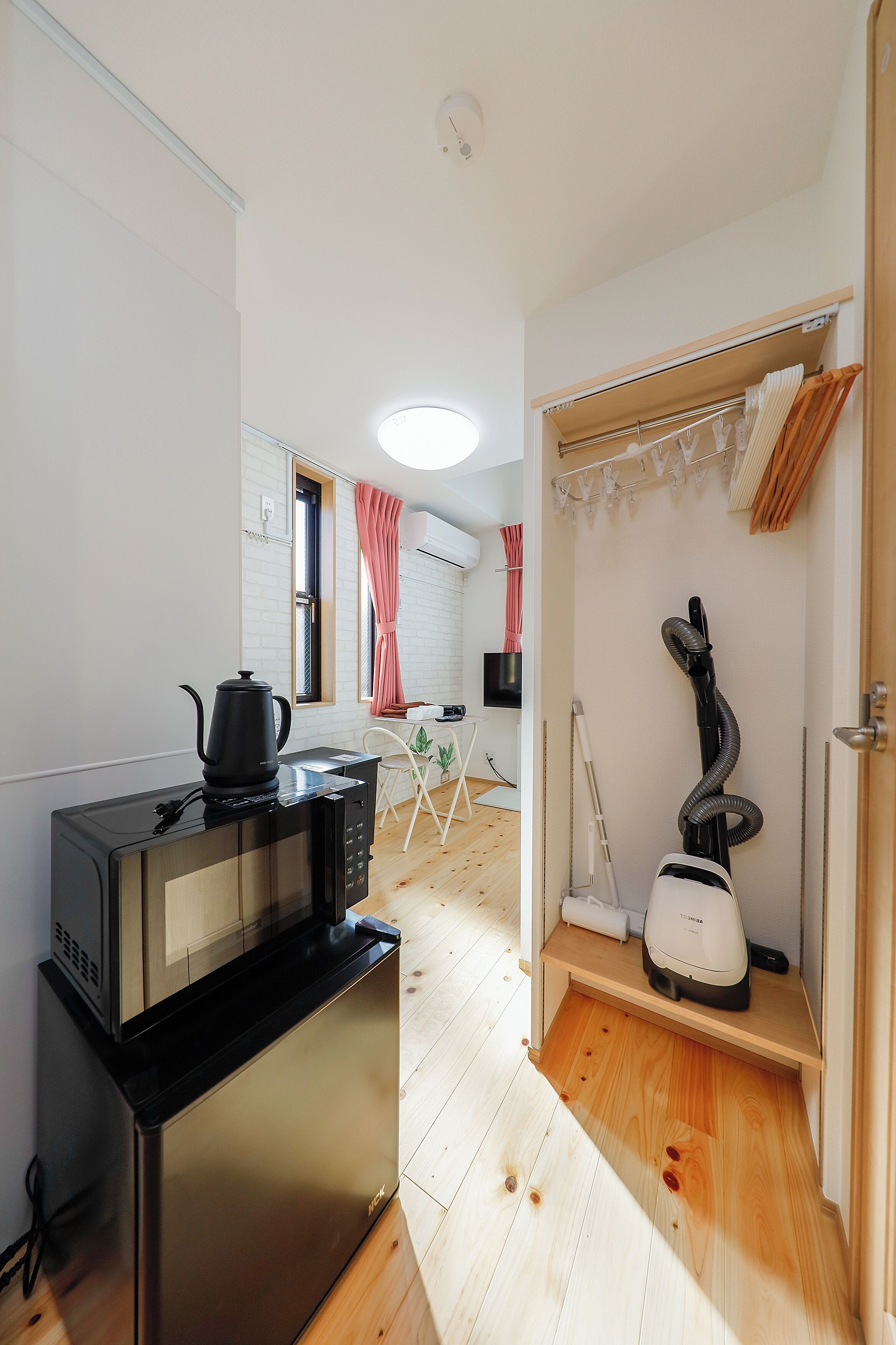 A compact kitchen with a microwave, kettle, and vacuum cleaner.