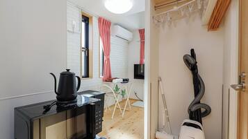 A compact kitchen with a microwave, kettle, and vacuum cleaner.