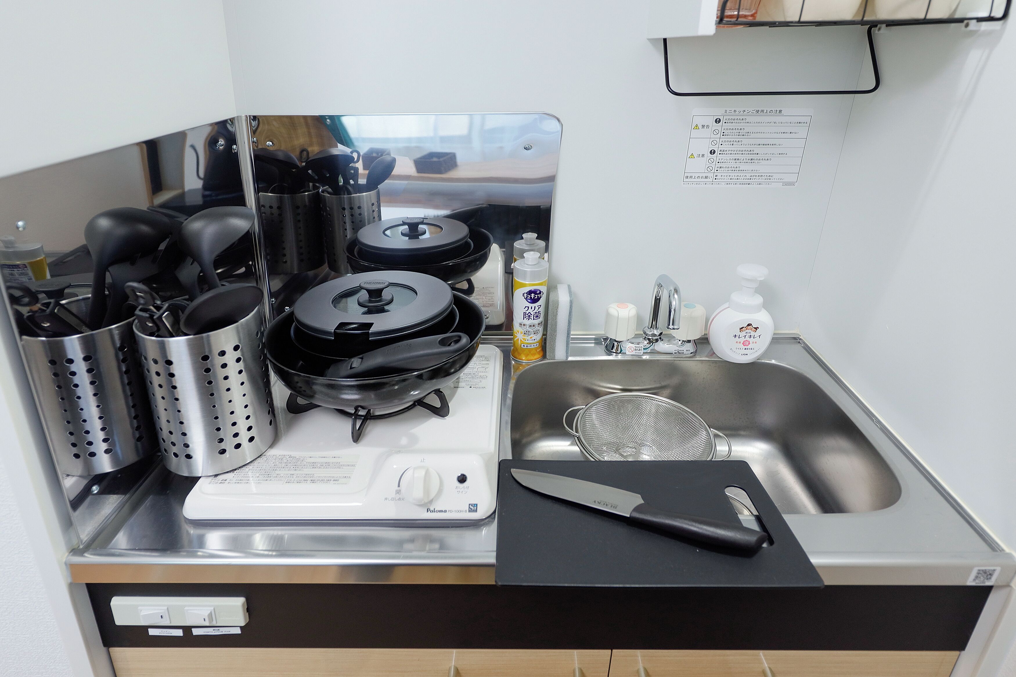 A compact kitchen with a stove, pots, a sink, and a cutting board.