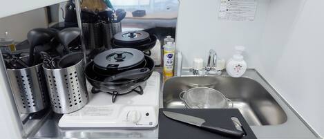 A compact kitchen with a stove, pots, a sink, and a cutting board.