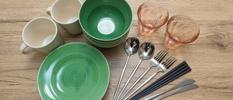 A wooden table with various dishes and utensils, including green plates, white cups, and pink glasses.