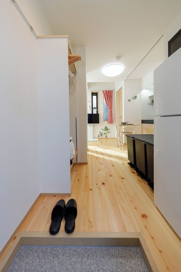 A narrow hallway with a wooden floor leading to a kitchen area. A pair of black shoes is placed on a small rug at the end of the hallway. - Zenith Shinjuku Hinoki by Tranova (Tokyo)
