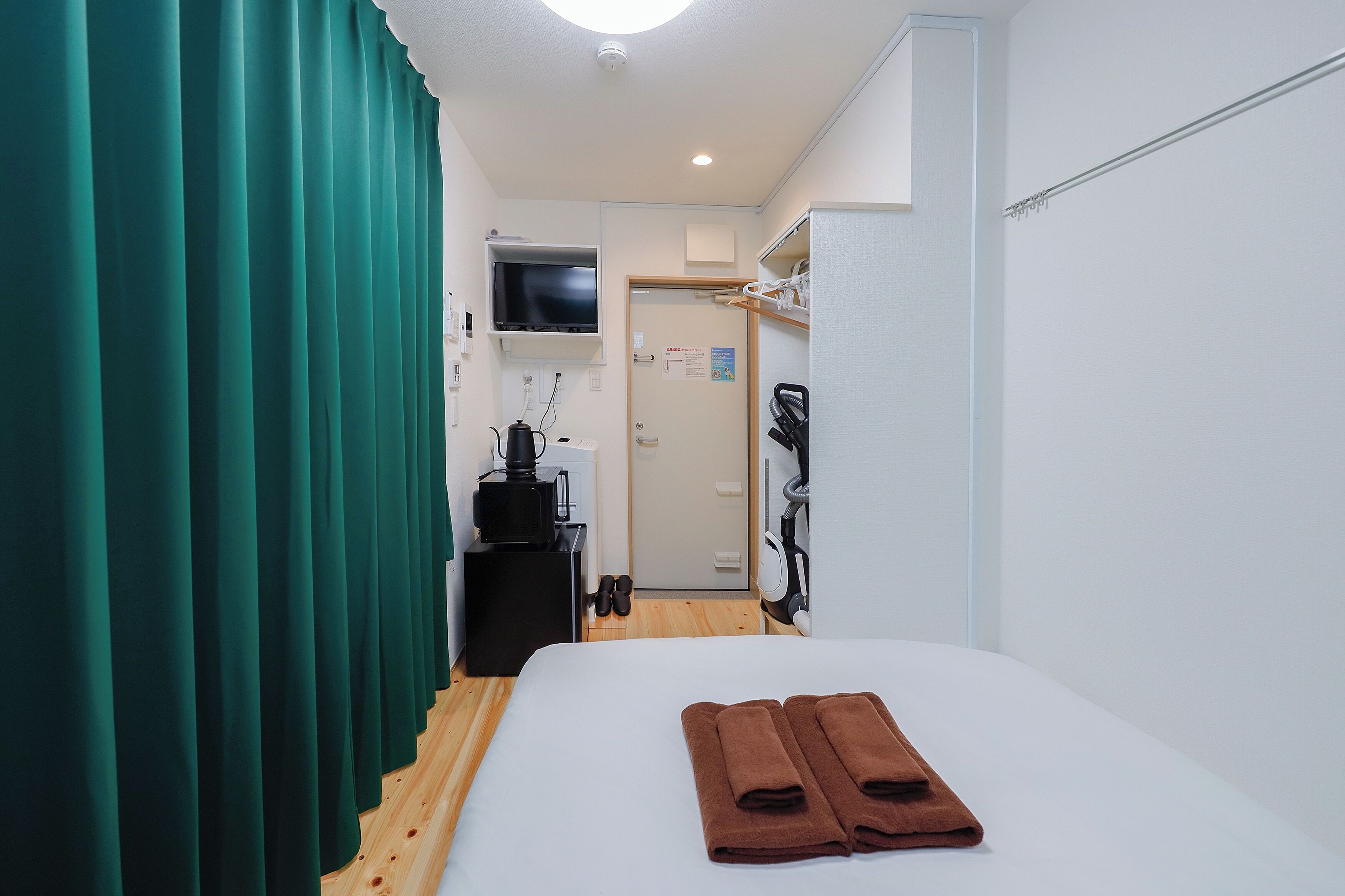 Una habitación de hotel con una cama, televisión, escritorio con hervidor y armario.