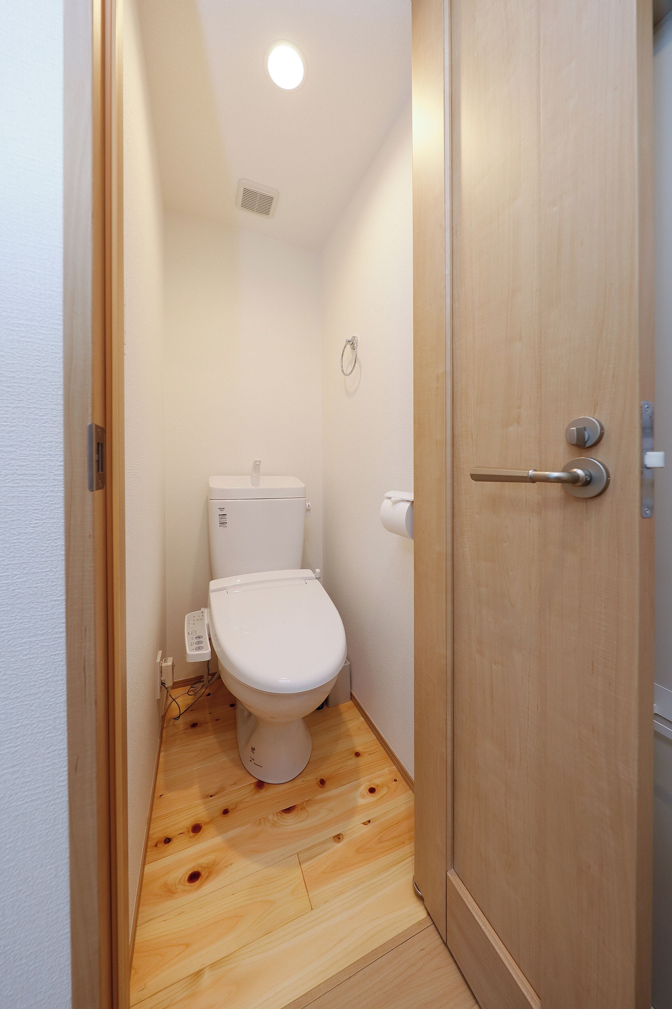 Une petite salle de bain compacte avec un plancher en bois, des toilettes blanches et une porte en bois.