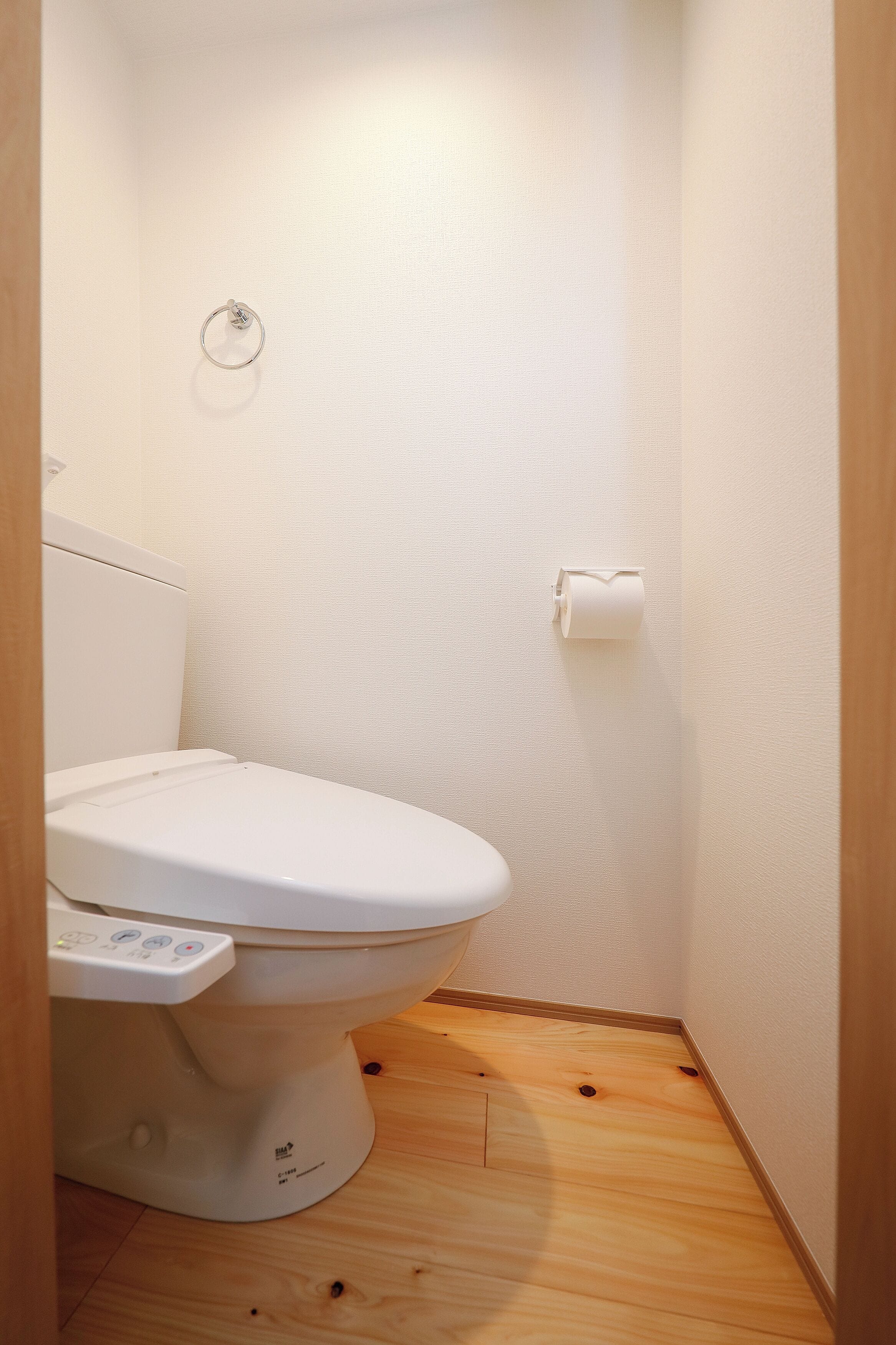 Un baño pequeño y moderno con inodoro, un dispensador de papel higiénico y piso de madera.