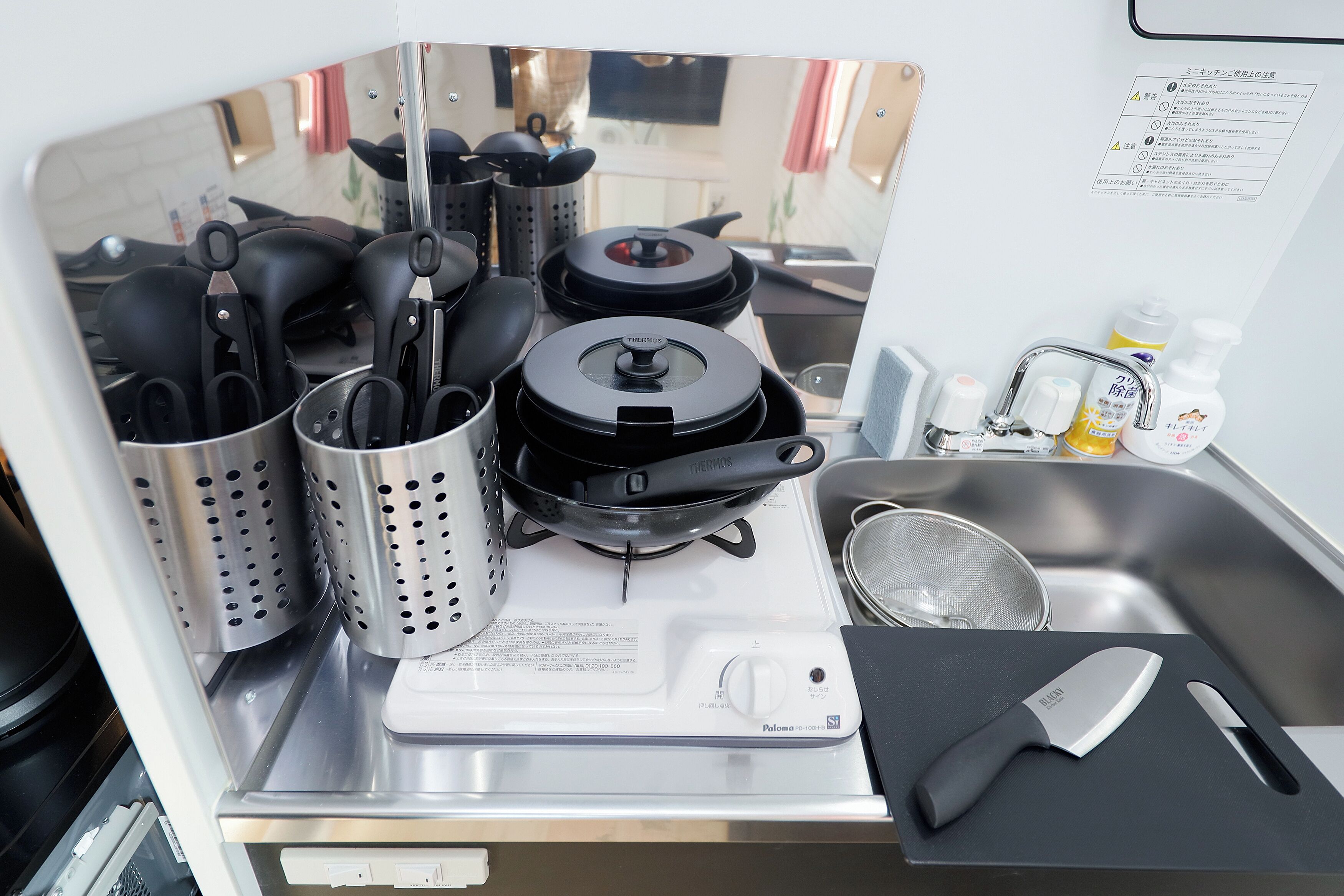 A kitchen with a stove, pots, a colander, a strainer, and a knife on a cutting board.