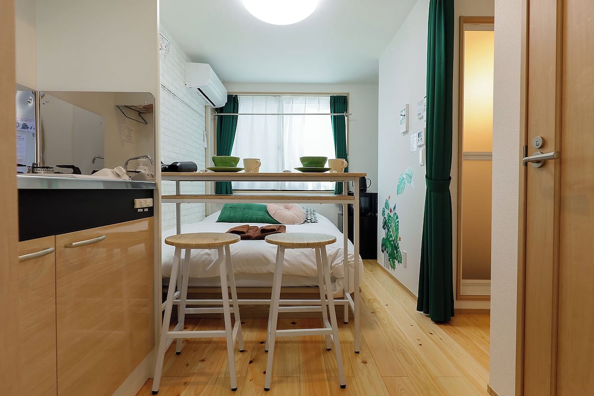 A compact room with a bunk bed, a small kitchen area, and a wooden floor.