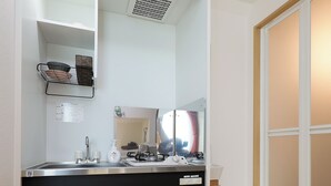 A compact kitchen with a built-in stove, a sink, and a mirror above it. There is a small shelf with a few items and a potted plant near the window. - Zenith Shinjuku Hinoki by Tranova (Tokyo)