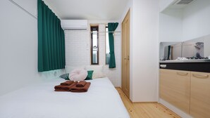 A bedroom with a bed, green curtains, a window, a wooden wardrobe, and a white brick wall. - Zenith Shinjuku Hinoki by Tranova (Tokyo)