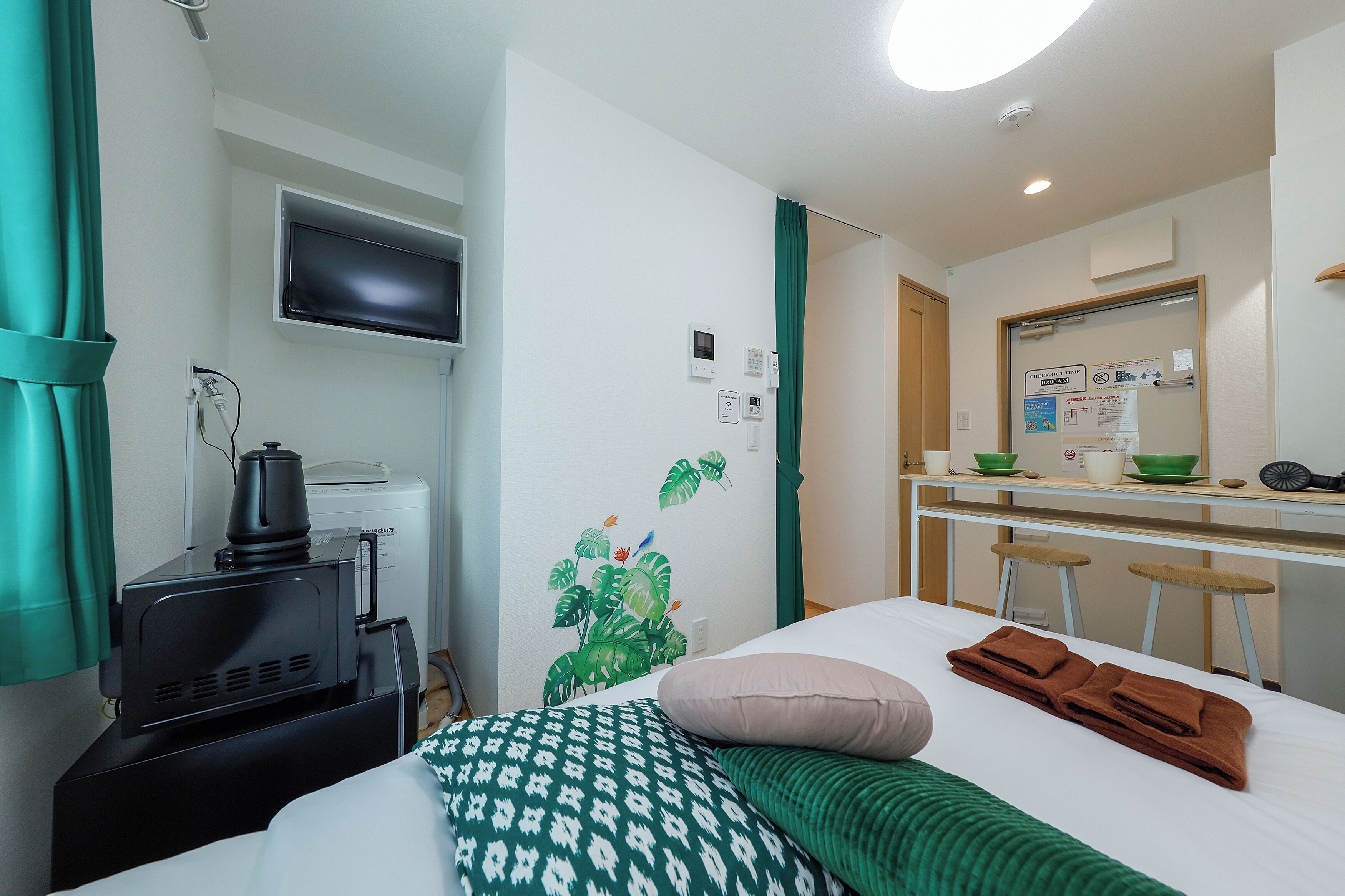 Habitación de hotel con cama, televisión, microondas, pequeña cocina y baño visible a través de una puerta.
