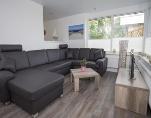 A modern living room with a large L-shaped sectional sofa, a wooden coffee table, and a television on a stand. - Holiday Home for 6 in Sint Maartenszee (Sint Maartensvlotbrug)