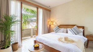 Ein Hotelzimmer mit einem Bett, einem Nachttisch mit Zitronen in einer Schale, einer Zimmerpflanze und Blick auf grüne Vegetation draußen.