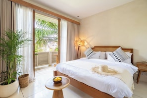 Une chambre d’hôtel avec un lit, une table de chevet sur laquelle se trouve un bol de citrons, une plante en pot et une vue sur la verdure à l’extérieur.