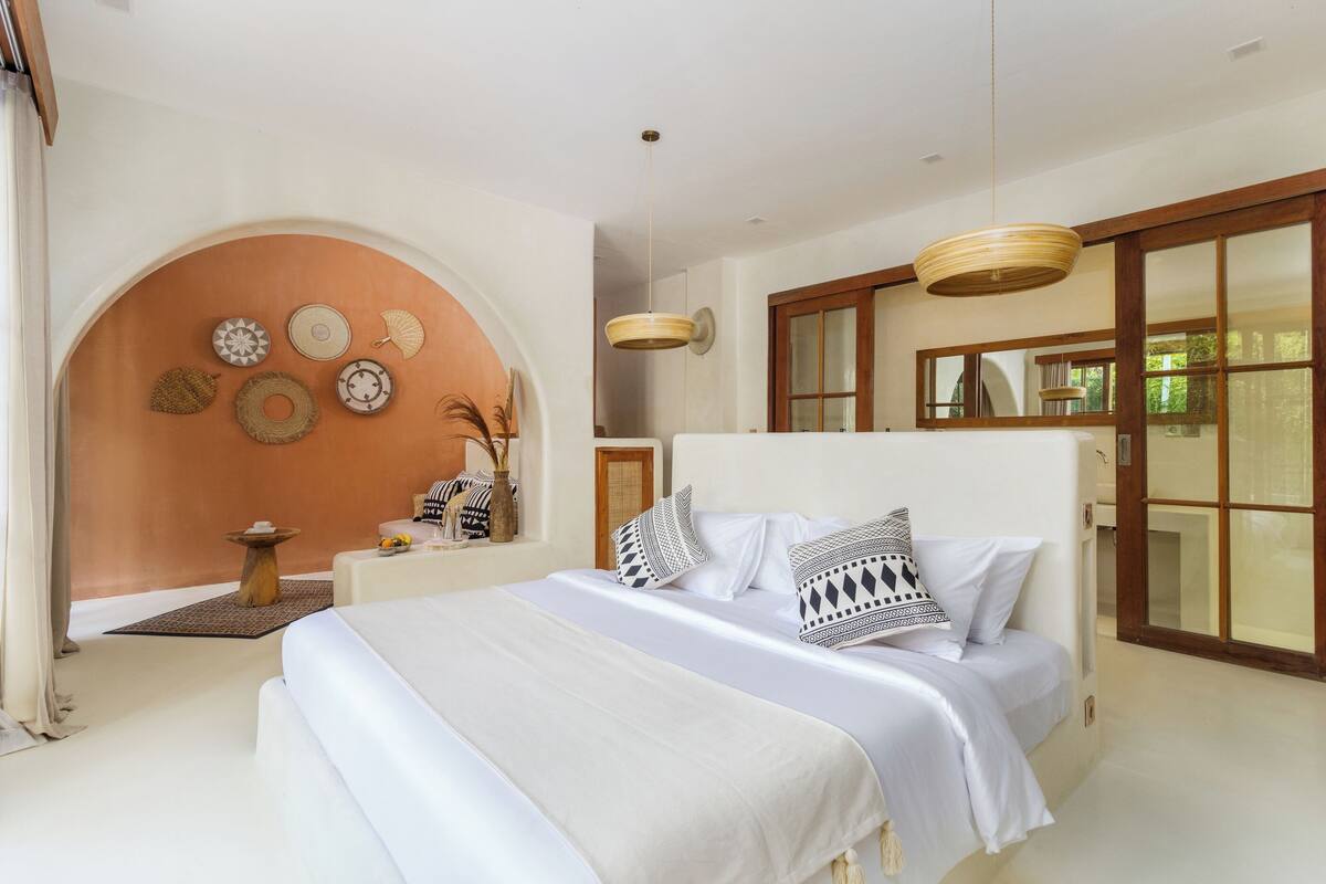 Een ruime slaapkamer met een groot bed, een houten nachtkastje en een decoratieve wand met diverse objecten.