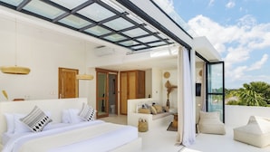 Une chambre moderne avec un grand lit, un canapé et un balcon doté d’un plafond en verre.
