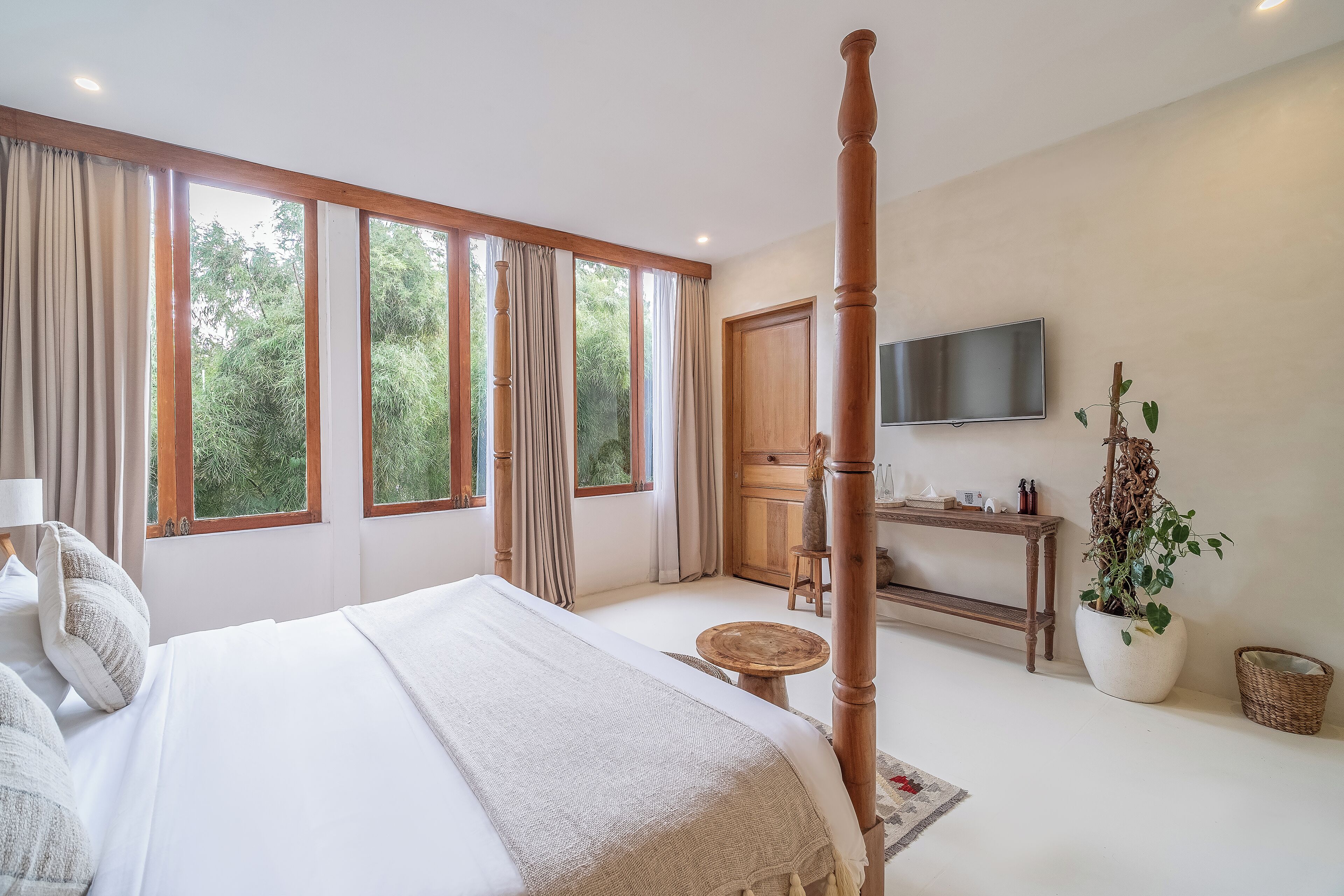A bedroom with a large bed, a wooden floor, a TV, a desk, and a window with curtains.