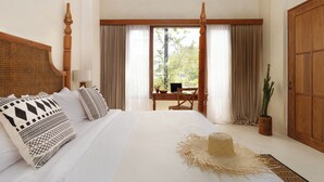 Ein Hotelzimmer mit einem großen Bett, einem Holzkopfstück, einem Schreibtisch mit einem Laptop, einer Zimmerpflanze und Blick auf Grünfläche.