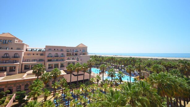A resort with multiple buildings, a swimming pool, and a beach view.