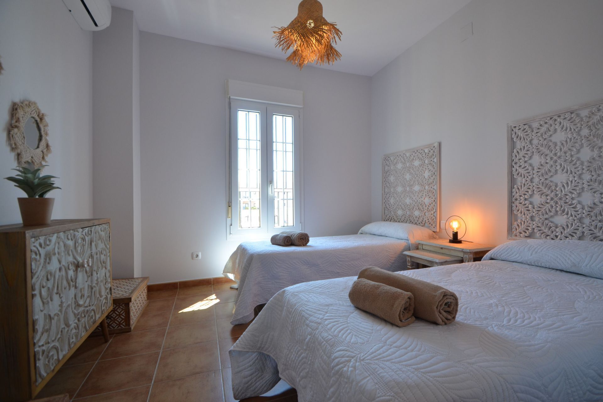 Une chambre avec deux lits, une fenêtre, un panneau décoratif au mur et une lampe de chevet.