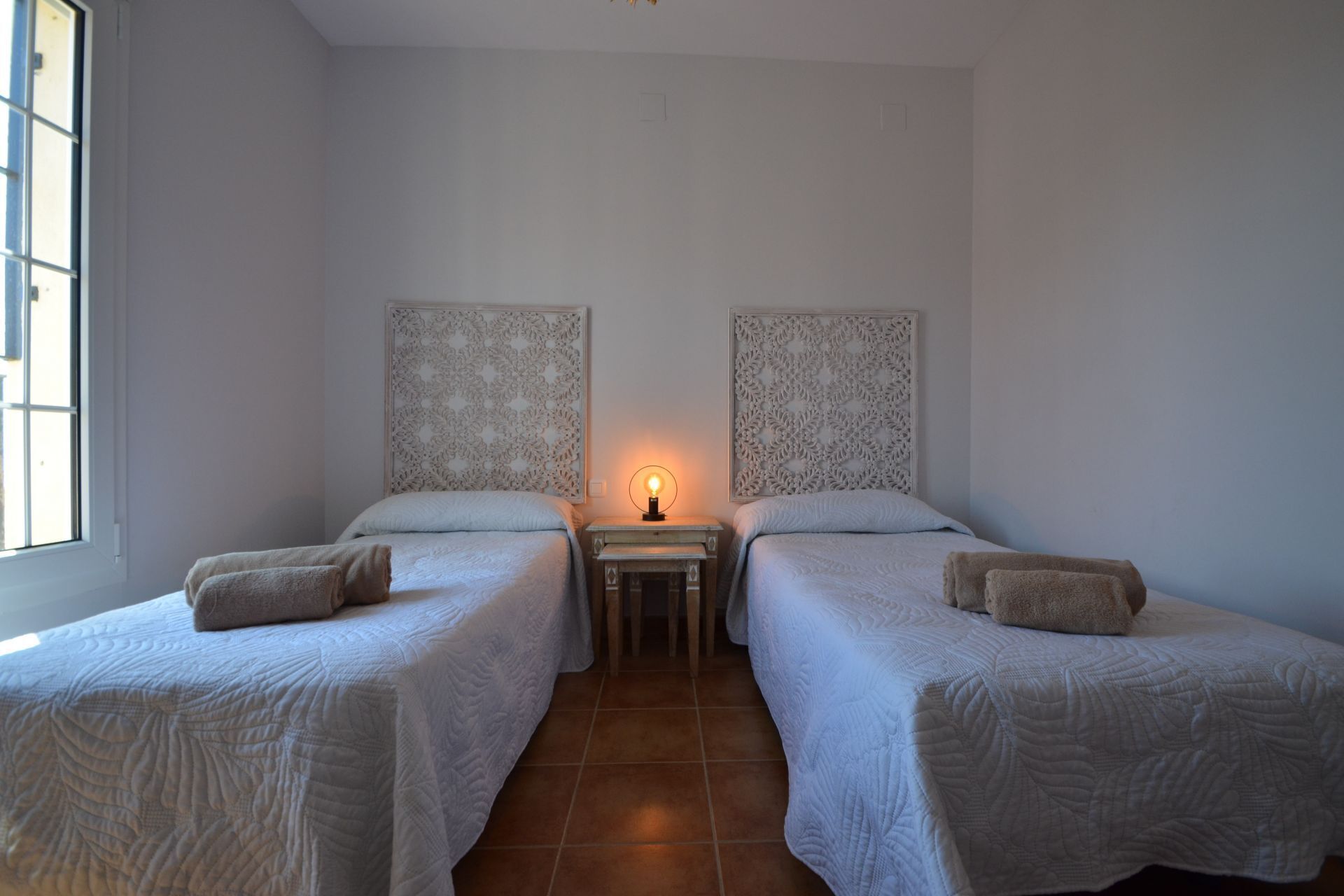 A room with two single beds, a small table with a lamp, and a window.