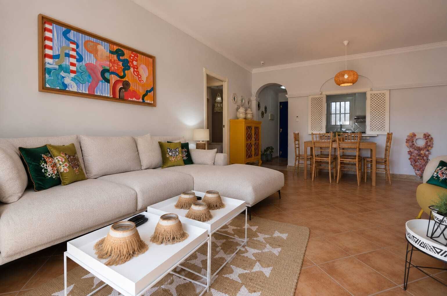 A modern living room with a sofa, coffee table, and a dining area with chairs and a table.