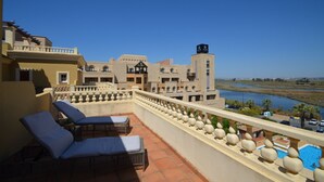 A hotel balcony with lounge chairs, a pool, and a view of a river and distant buildings.