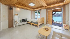 A room with a bed, a TV, a wooden table, a mirror, and a view of the sea. - Namhae Bada Yanolja Pension (Namhae)