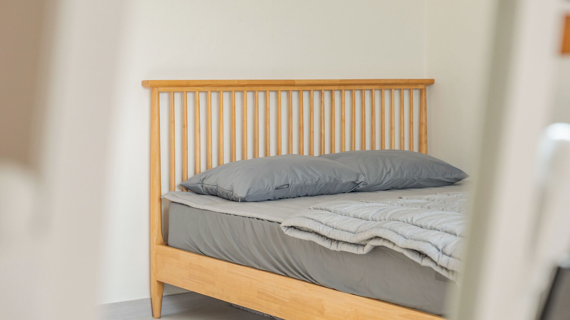 Una cama individual con cabecera de madera y ropa de cama gris.